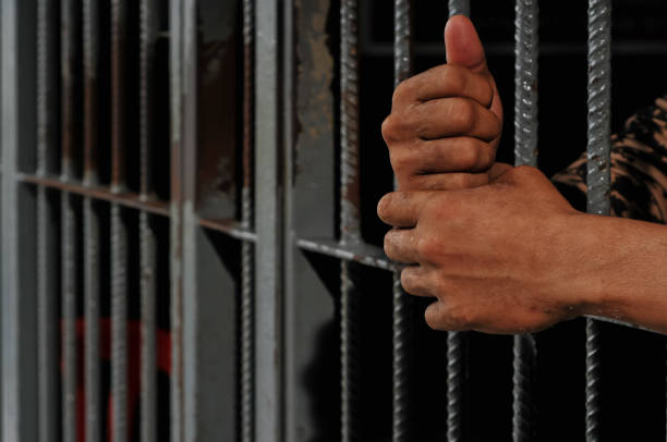 istock hands of a prisoner behind prison bars on black background 2169023651