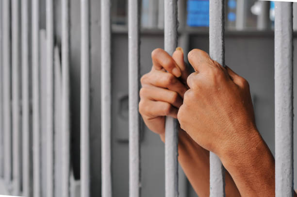 istock hands of a prisoner behind prison bars on black background 2169023695