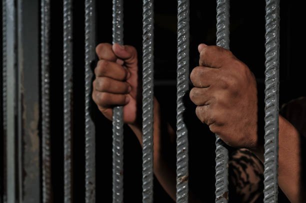 istock hands of a prisoner behind prison bars on black background 2169023703