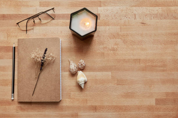 Journaling setup with notebook, candle, seashells, and eyeglasses on wooden surface with copy space
