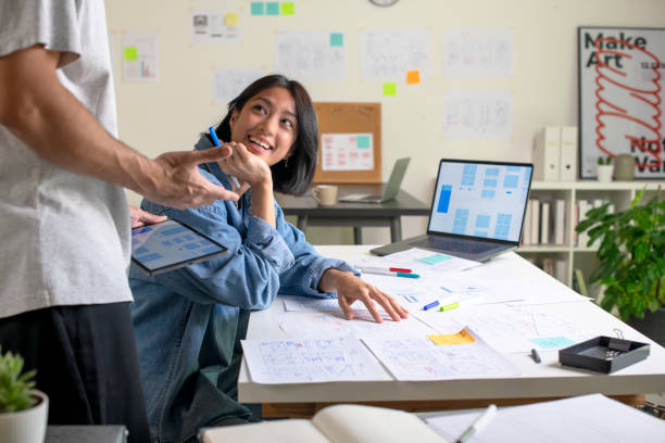 istock UX/UI designers discussing and brainstorming on wireframes for a website and mobile app prototype, surrounded by sketches of user flow and design tools, in the concept of website and mobile application design concept. 2169040277