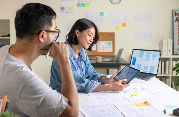 istock UX/UI designers discussing and brainstorming on wireframes for a website and mobile app prototype, surrounded by sketches of user flow and design tools, in the concept of website and mobile application design concept. 2169040278