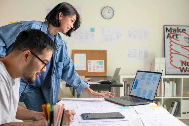istock UX/UI designers discussing and brainstorming on wireframes for a website and mobile app prototype, surrounded by sketches of user flow and design tools, in the concept of website and mobile application design concept. 2169040280