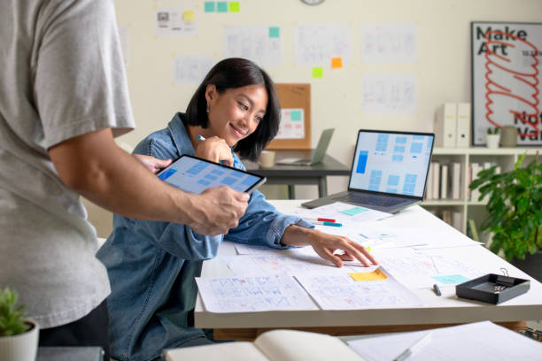 istock UX/UI designers discussing and brainstorming on wireframes for a website and mobile app prototype, surrounded by sketches of user flow and design tools, in the concept of website and mobile application design concept. 2169040282