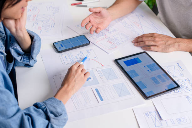 istock UX/UI designers discussing and brainstorming on wireframes for a website and mobile app prototype, surrounded by sketches of user flow and design tools, in the concept of website and mobile application design concept. 2169040403