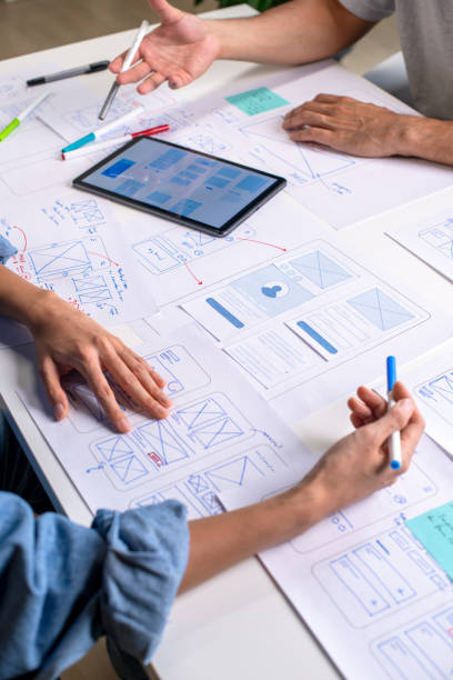 istock UX/UI designers discussing and brainstorming on wireframes for a website and mobile app prototype, surrounded by sketches of user flow and design tools, in the concept of website and mobile application design concept. 2169040409