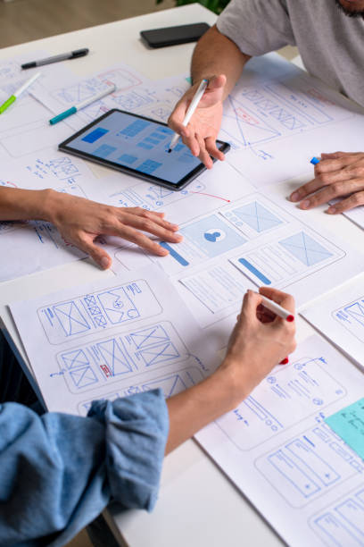 istock UX/UI designers discussing and brainstorming on wireframes for a website and mobile app prototype, surrounded by sketches of user flow and design tools, in the concept of website and mobile application design concept. 2169040412