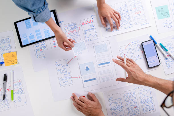 istock UX/UI designers discussing and brainstorming on wireframes for a website and mobile app prototype, surrounded by sketches of user flow and design tools, in the concept of website and mobile application design concept. 2169040416