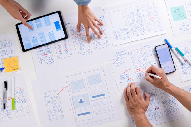 designéři ux/ui diskutují a brainstormují o wireframech pro prototyp webu a mobilní aplikace, obklopeni skicami toku uživatelů a návrhových nástrojů, v konceptu konceptu designu webových stránek a mobilních aplikací. - plán na papíře - stock snímky, obrázky a fotky