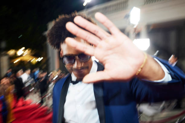 Blurred motion of young male celebrity blocking cameras at event. Man is shielding himself from paparazzi. He is wearing tuxedo.