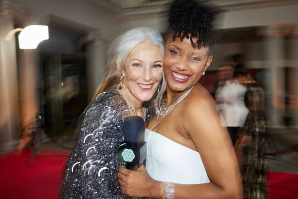 Portrait of smiling host with mature actress at red carpet event. Happy women at film festival. They are looking at camera.