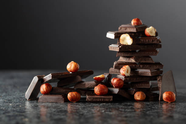 istock Broken dark chocolate bar with hazelnuts on a black background. 2169045195