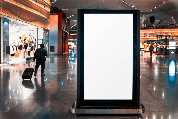 Empty airport ad screen template A modern airport terminal with a large digital advertising screen mockup - a blank white space in the foreground. A silhouette of a traveler pulling a suitcase walks past a fashion retail store retail digital signage stock pictures, royalty-free photos & images