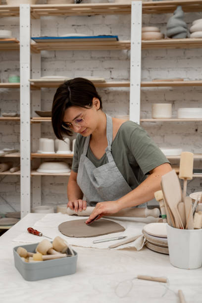 istock Slab building method in ceramics crafting. Using a wooden stick to roll out a flat sheet of clay. Preparing clay for cutting and assembling it. 2169065999