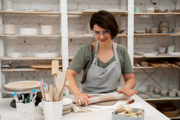 istock Slab building method in ceramics crafting. Using a wooden stick to roll out a flat sheet of clay. Preparing clay for cutting and assembling it. 2169066001