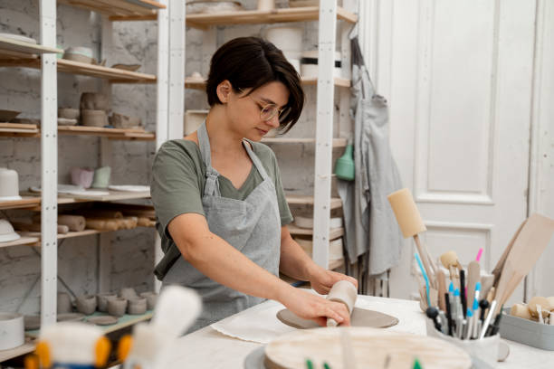 istock Slab building method in ceramics crafting. Using a wooden stick to roll out a flat sheet of clay. Preparing clay for cutting and assembling it. 2169066895