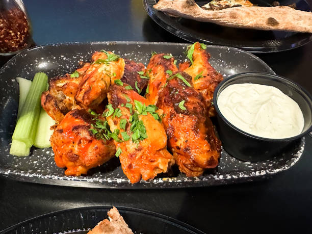 A platter featuring spicy chicken wings garnished with fresh herbs, accompanied by celery sticks and blue cheese  sauce