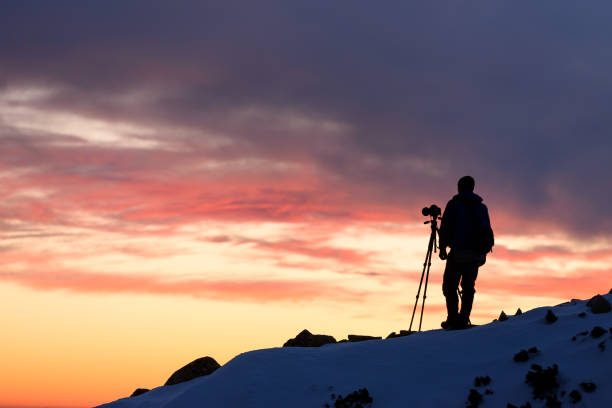 Landscape photographer with a tripod shooting in the mountains at sunset