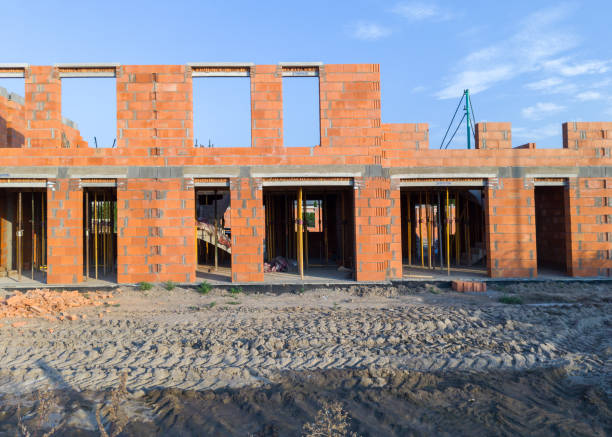 View of a construction site with partially built brick walls of a new building, under a clear sky.