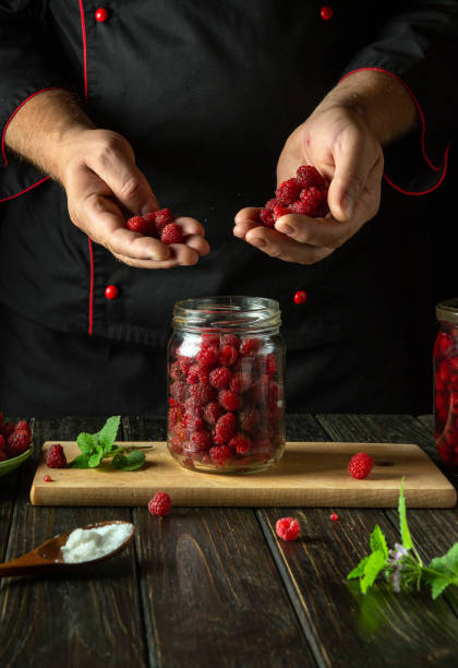 istock Chef hands sorting raspberries before filling a canning jar. Making Rubus idaeus compote on a kitchen counter. Advertising space 2169096417