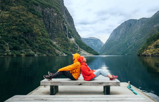 istock Happy couple dressed bright windproof jackets sitting back to back on bench on the Norwegian Nærøyfjord bank in Gudvangen, Norway. Traveling, beauty in Nature and relations concept. 2169104398