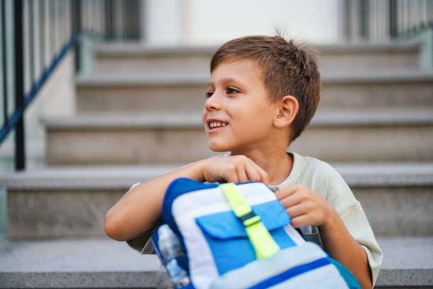 A young boy sits on steps with a backpack, smiling and ready for his first day at school. Capturing the excitement of a new school year and childhood beginnings.