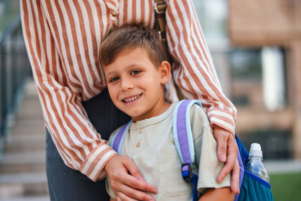 istock Happy Young Boy with Backpack Hugs Mom Before School 2169109424