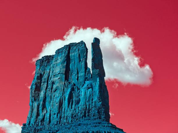 Mittens butte in Monument Valley Arizona. Image processed with inverse IR filter producing cool toned sandstone butte with red sky. The white cloud remains white in color.