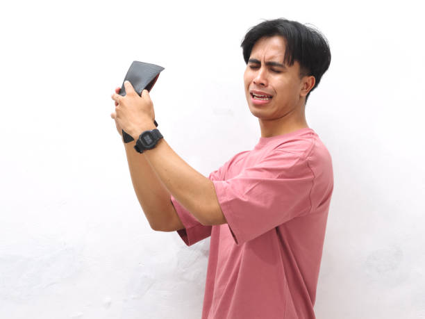 istock A young Asian man in a pink shirt holds an empty wallet with a sad expression on a white isolated background. 2169117579