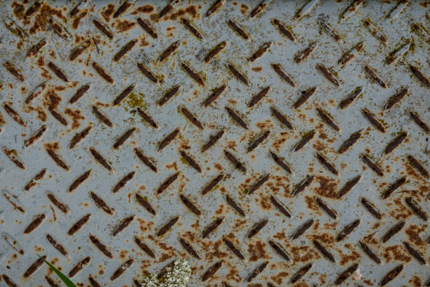 a rusted iron sheet featuring a distinct crisscross grip pattern, heavily marked by corrosion and decay. The surface is rough and uneven, with the rust penetrating deep into the metal, creating a mix of red, orange, and brown tones across the grid. The crisscross texture, originally designed for traction, now stands out as a prominent feature, contrasting with the surrounding weathered and tarnished metal