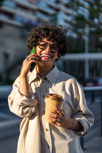 istock Smiling Woman Holding Coffee and Using Smartphone Outdoor 2169132307