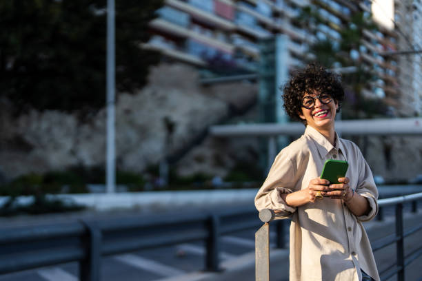 istock Smiling Woman Engaging with Mobile Device in Urban Setting 2169132336