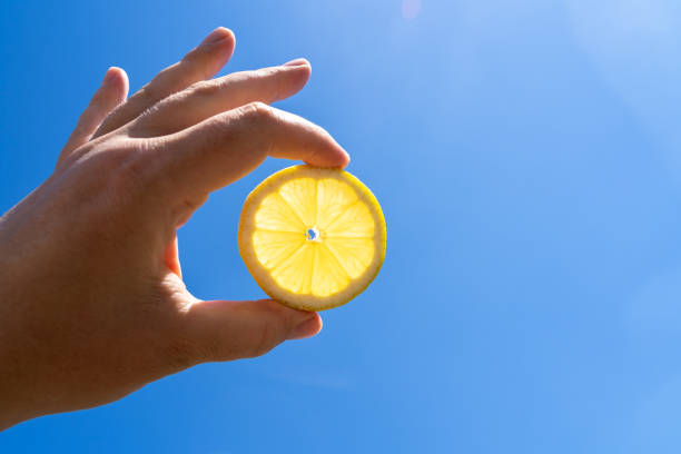 Hand holding lemon in the blue sunny sky