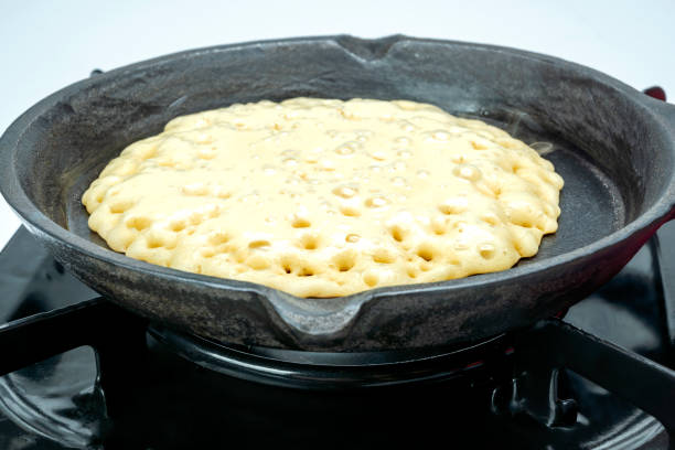 A pan of batter is cooking on a stove. The batter is bubbly and has a lot of holes