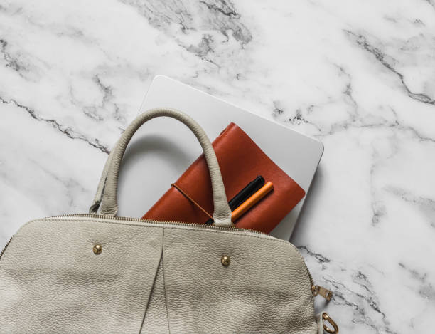 istock Women's beige leather bag, laptop, notebook, pen on marble background, top view 2169173252
