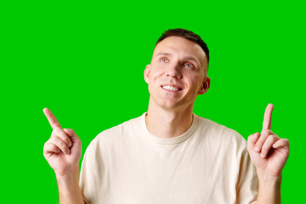 istock Young Man Pointing Upward While Smiling Against a Bright Green Background 2169173551