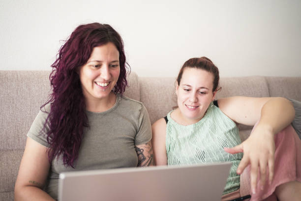 istock Two sisters sitting on a couch, looking at a laptop 2169180108