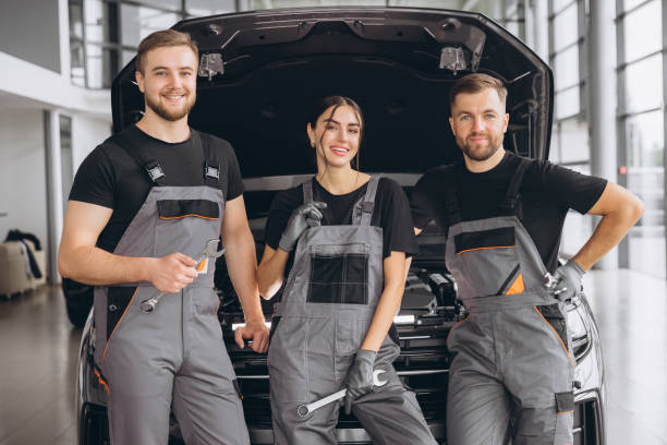 istock Three smiling workers, mechanics two men and woman in grey uniform standing at open hood, garage vehicle shop, auto mechanic technician maintenance customer car automobile at repair service. 2169183105