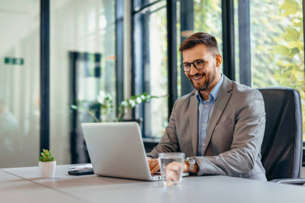 istock Businessman working on laptop in modern office with large windows. 2169189050