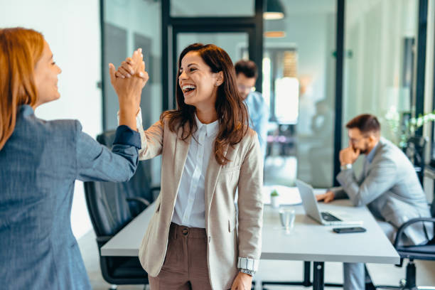 Two professional women celebrating success in a modern office space.