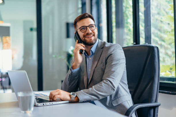 istock Focused professional man smiling while talking on smartphone in bright modern office 2169191946