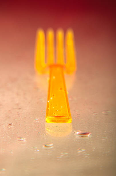 Yellow plastic fork and drops of water on a glass surface. Tabled.