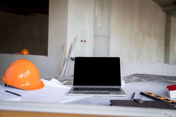 istock Laptop with helmet, blueprint and architects house model on desk in construction site. 2169197389