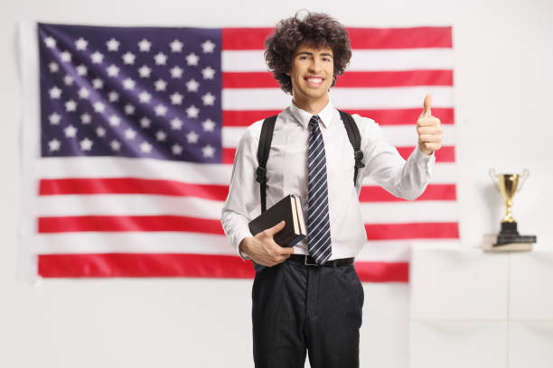 College student holding books and showing thumbs up in front of an american flag