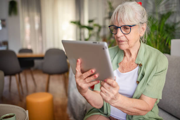 istock Elderly woman focused on a tablet while sitting on sofa 2169210573