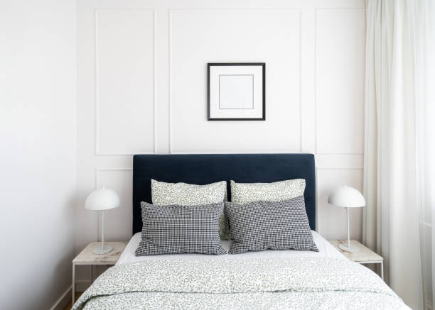 istock Modern bedroom with a navy headboard, patterned pillows, and soft lighting in a bright, airy space 2169211019