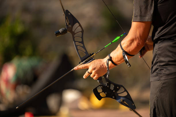 A man is holding a bow and arrow, pointing it at a target