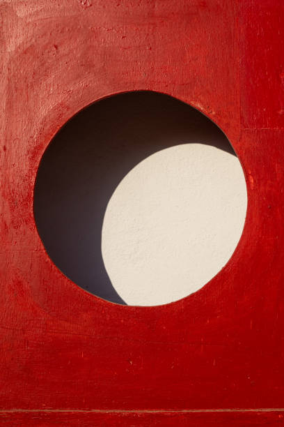 Detail of a  bright red case with a circle hole, prepared for a fire extinguisher. Empty in this case. Sunlight and shadow creating a shape of moon. Djerba, Tunisia, Africa.