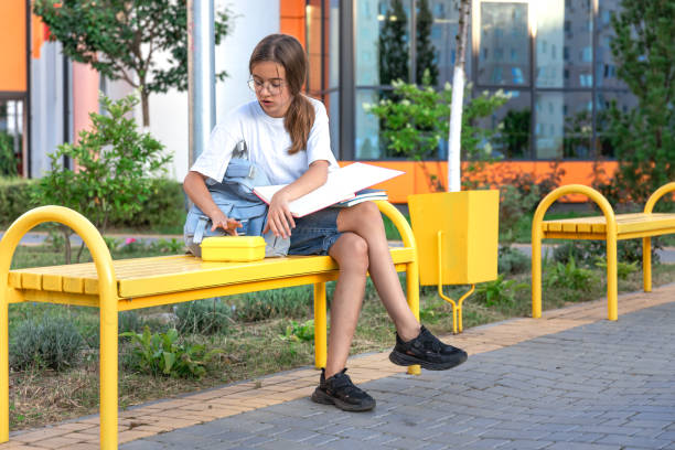 istock The student is sitting on a bench with a lunch box. Student with school supplies. Background school. 2169214948