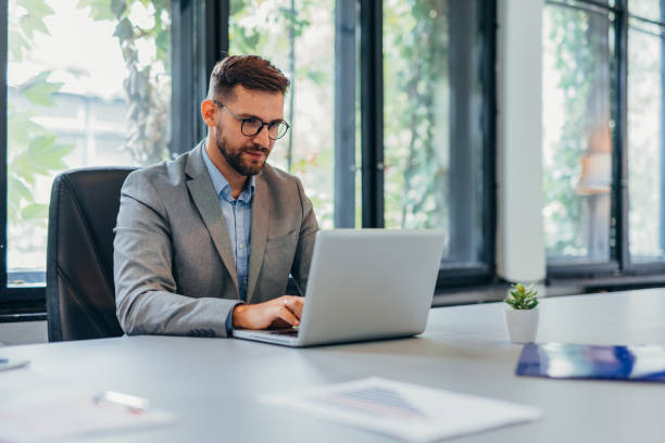 istock Businessman working on laptop in modern office with large windows. 2169215331